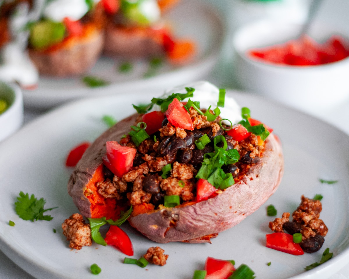 Close up of a Mexican stuffed sweet potato on a serving plate that is loaded with a turkey and black bean taco filling and all kinds of delicious taco toppings.