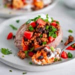 Close up of a taco loaded sweet potato on a serving plate that is loaded with a turkey and black bean taco filling and all kinds of delicious taco toppings.