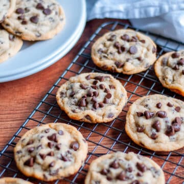 Freshly baked egg free chocolate chip cookies on a wire cooling rack with a plate of cookies and white linen beside it.