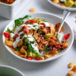 Close up of a white serving plate with a scoop of walking taco casserole topped with lettuce, tomatoes, avocado, and sour cream, with a fork holding a bite.