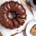 Top-down shot of a banana chocolate chip bundt cake with chocolate glaze with slices cut into the cake, and a separate slice on a plate next to the cake.