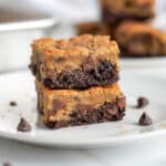 Two brookie bars stacked on top of each other on a white serving plate, with chocolate chips, crumbs, and more brookies around it.