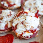 Close up of a freshly baked english muffin pizza half leaning on the other cooked mini pizzas on a parchment lined baking sheet.