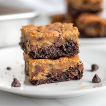 Feature image showing two brookie bars stacked on top of each other on a white serving plate, with chocolate chips, crumbs, and more brookies around it.